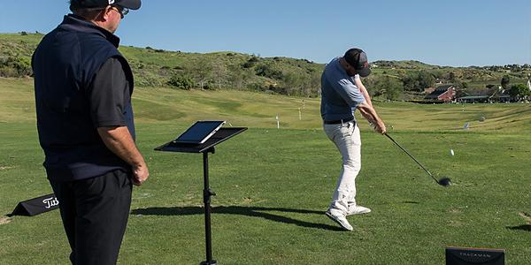 Golfer swinging golf club for ball flight monitor test with club fitting expert